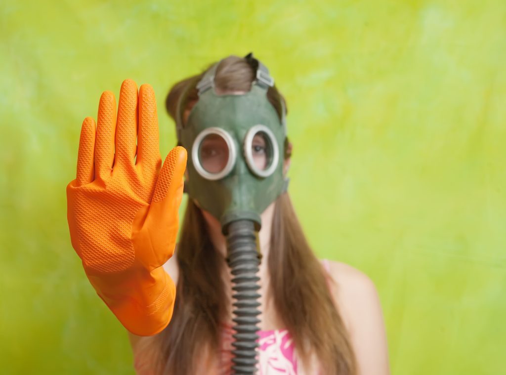 Femme portant un masque à gaz et un gant de nettoyage orange, levant la main en signe d'arrêt, contre les mauvaises odeurs ou la pollution.